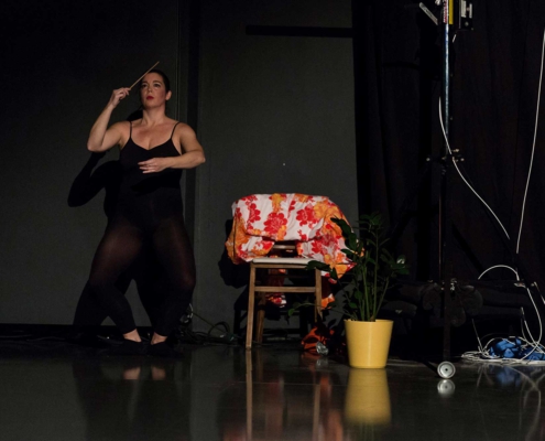 Pilar Murube während der Tanzperformance Corazón Partío auf der Bühne neben einem Stuhl und einer Pflanze.
