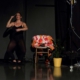 Pilar Murube während der Tanzperformance Corazón Partío auf der Bühne neben einem Stuhl und einer Pflanze.