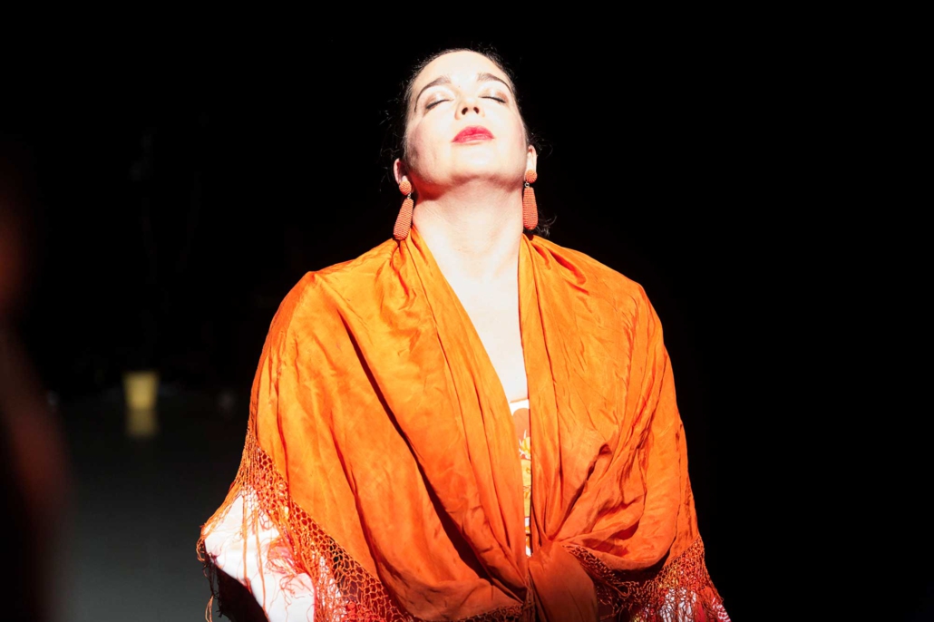 Pilar Murube – Corazón Partío Pilar Murube während der Tanzperformance Corazón Partío in einem orangefarbenen Kostüm auf der Bühne.